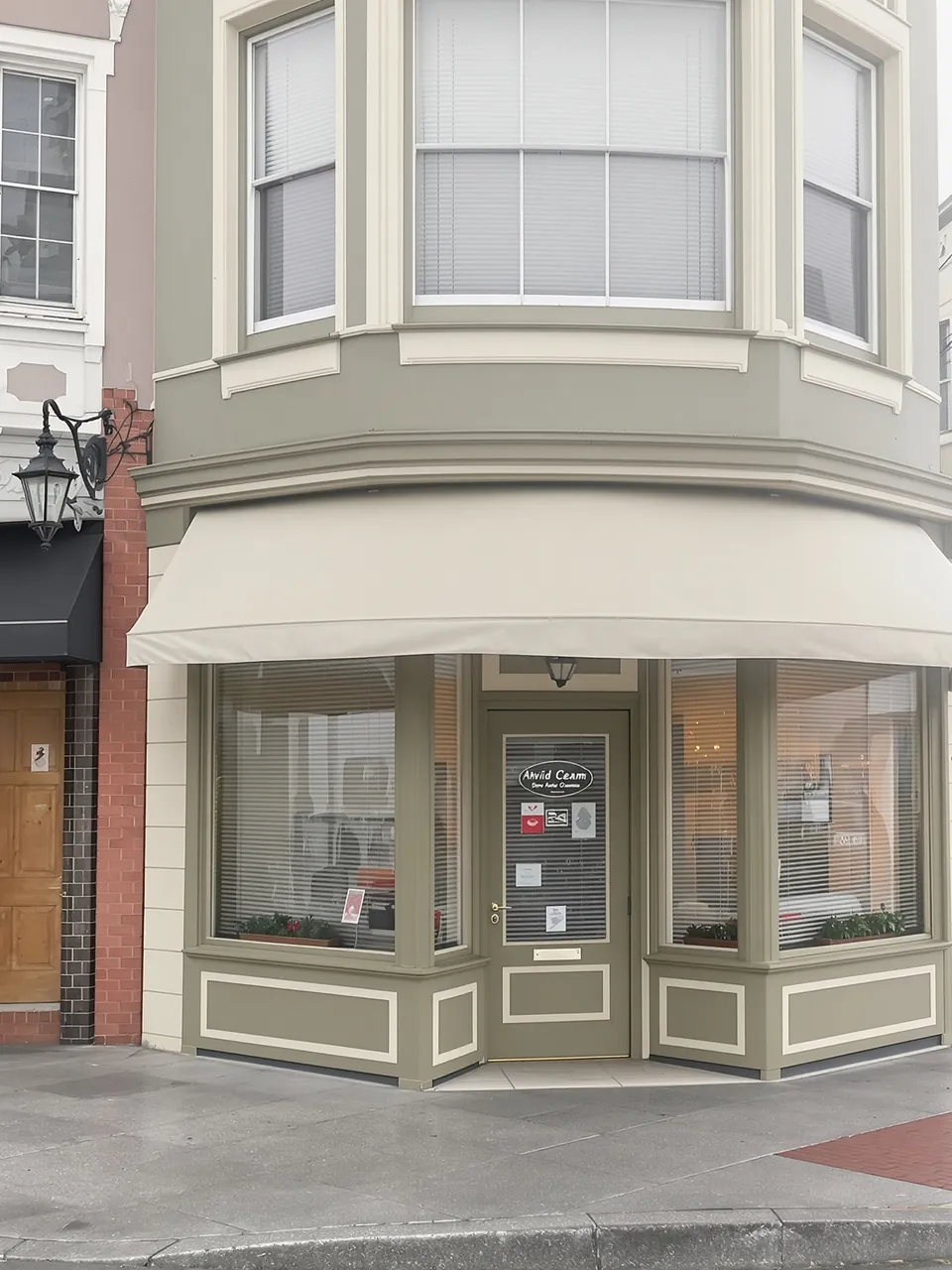 Corner storefront freshly painted olive green with cream trim and a plain canvas awning