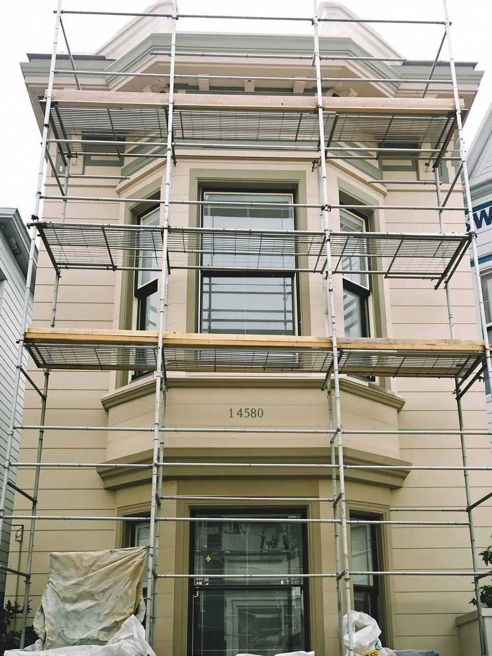 Aluminium scaffolding against the upper bay window of a Victorian being repainted cream